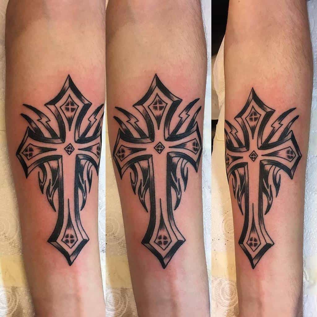 Tattoo of a cross with tribal flame designs on a forearm