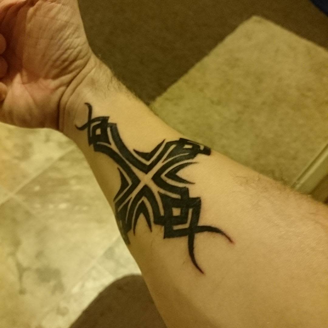 A striking forearm tattoo features a bold black tribal cross design