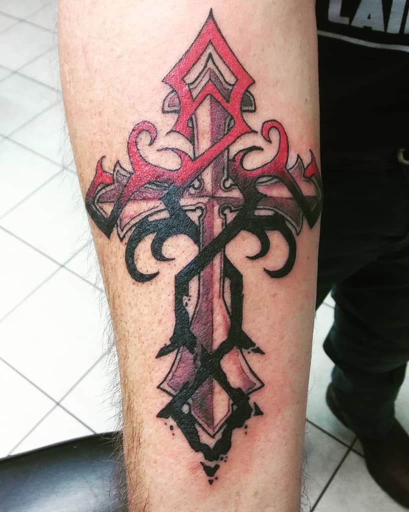 Forearm tattoo of an ornate cross elegantly blended with black and red tribal designs