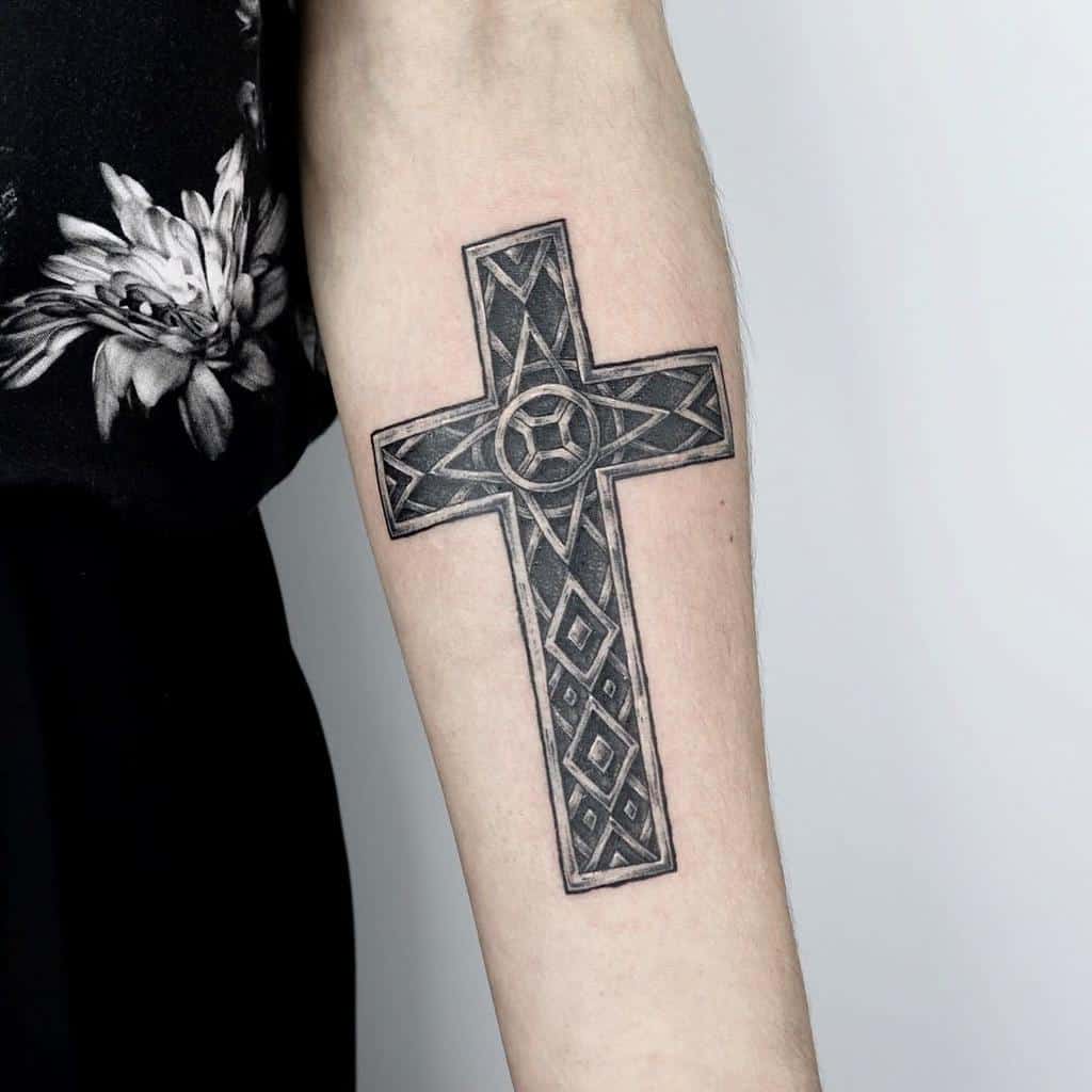 Tattoo of a detailed cross with geometric patterns on a person's forearm