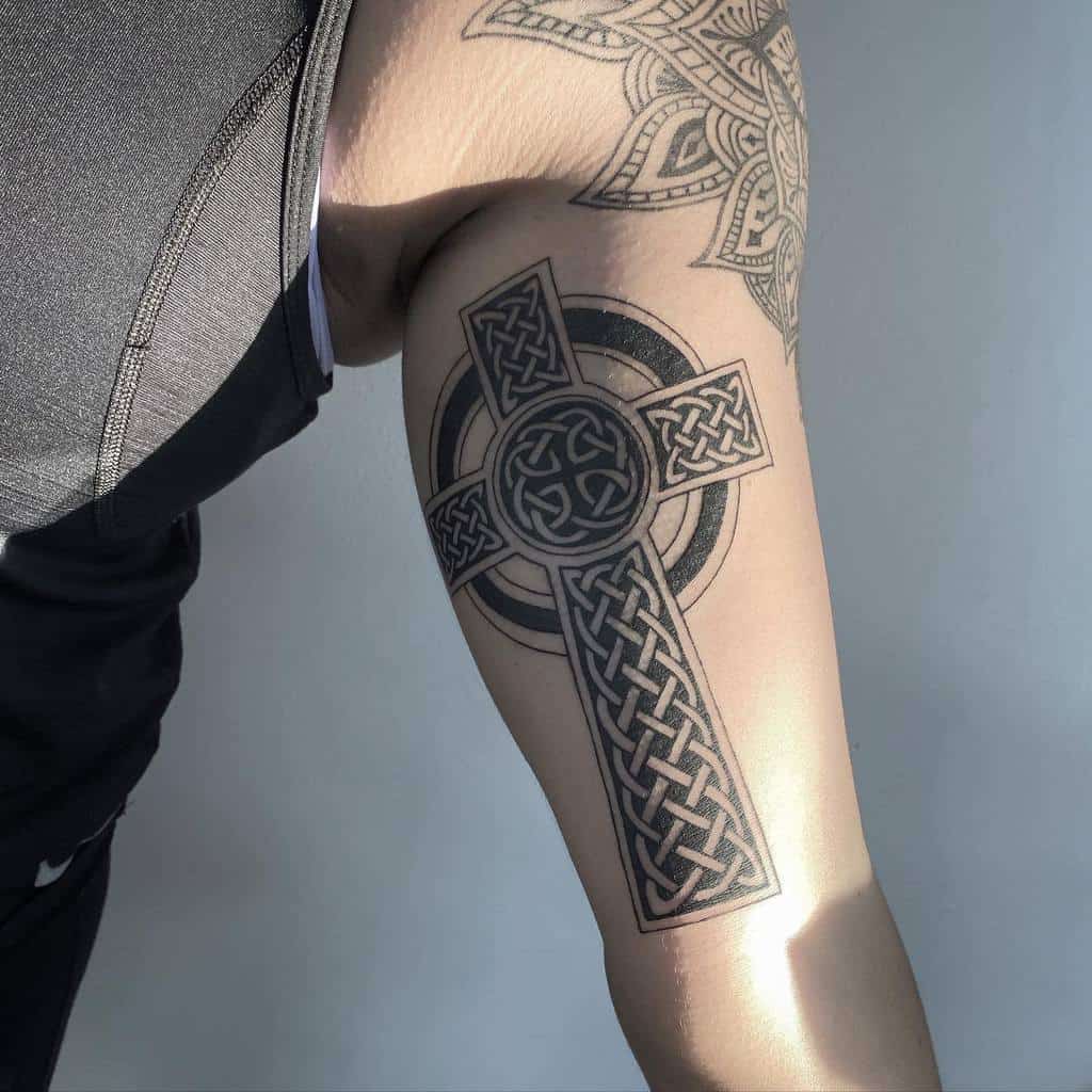 An arm displays a tattoo of a Celtic cross interwoven with intricate knot patterns