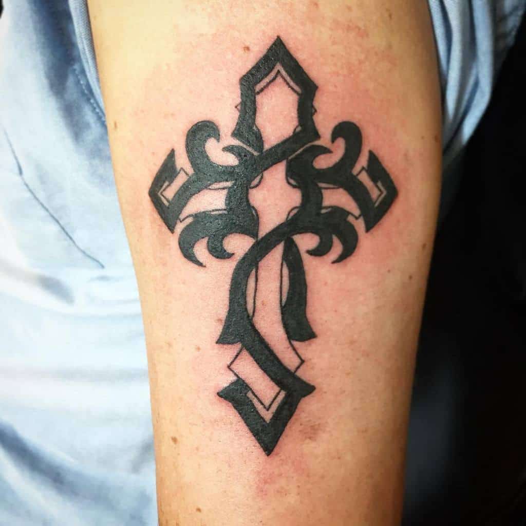 Intricate black cross tattoo with bold curves and sharp edges on the upper arm