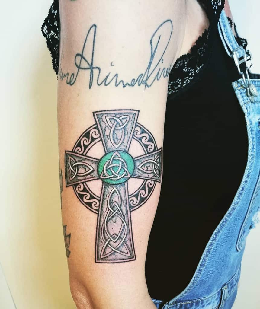 Detailed Celtic-style tribal cross tattoo on the upper arm, featuring knotwork patterns and a green centerpiece