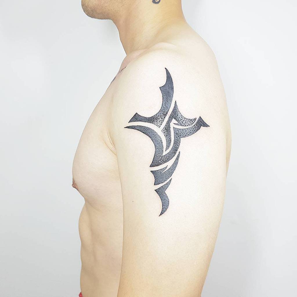 Tribal cross tattoo design in black ink on a man’s upper arm, featuring sharp, bold lines and geometric patterns