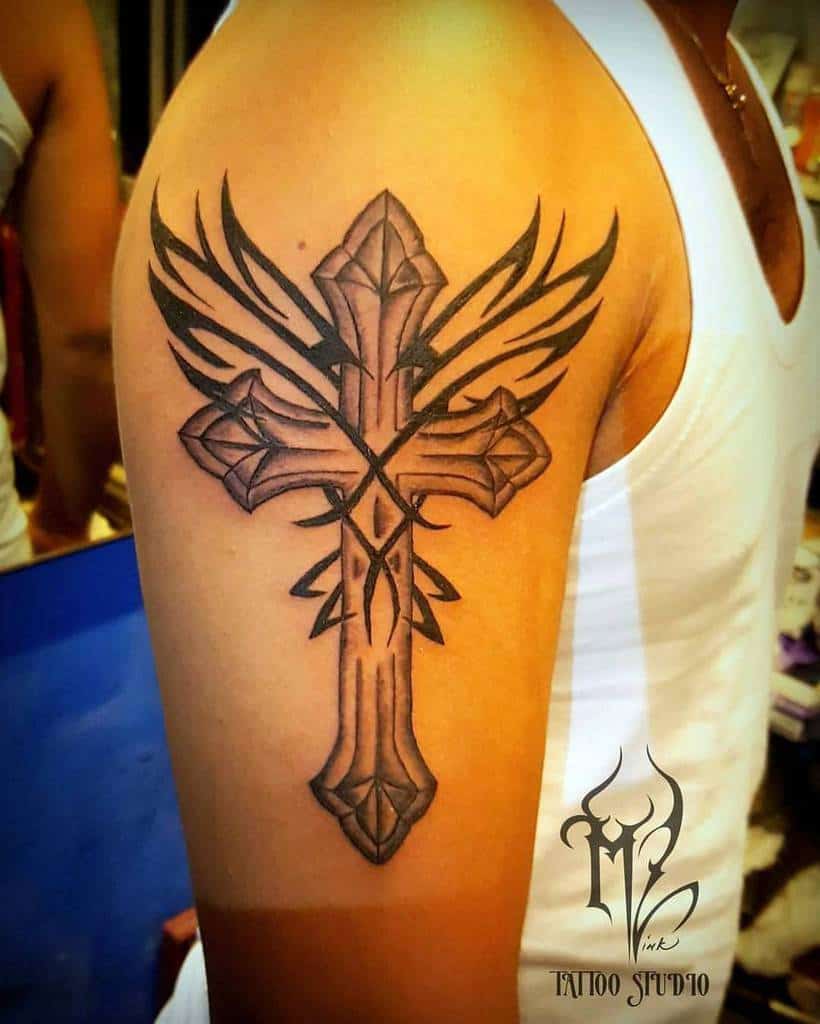 Tattoo of an ornate cross with wings on a person's upper arm