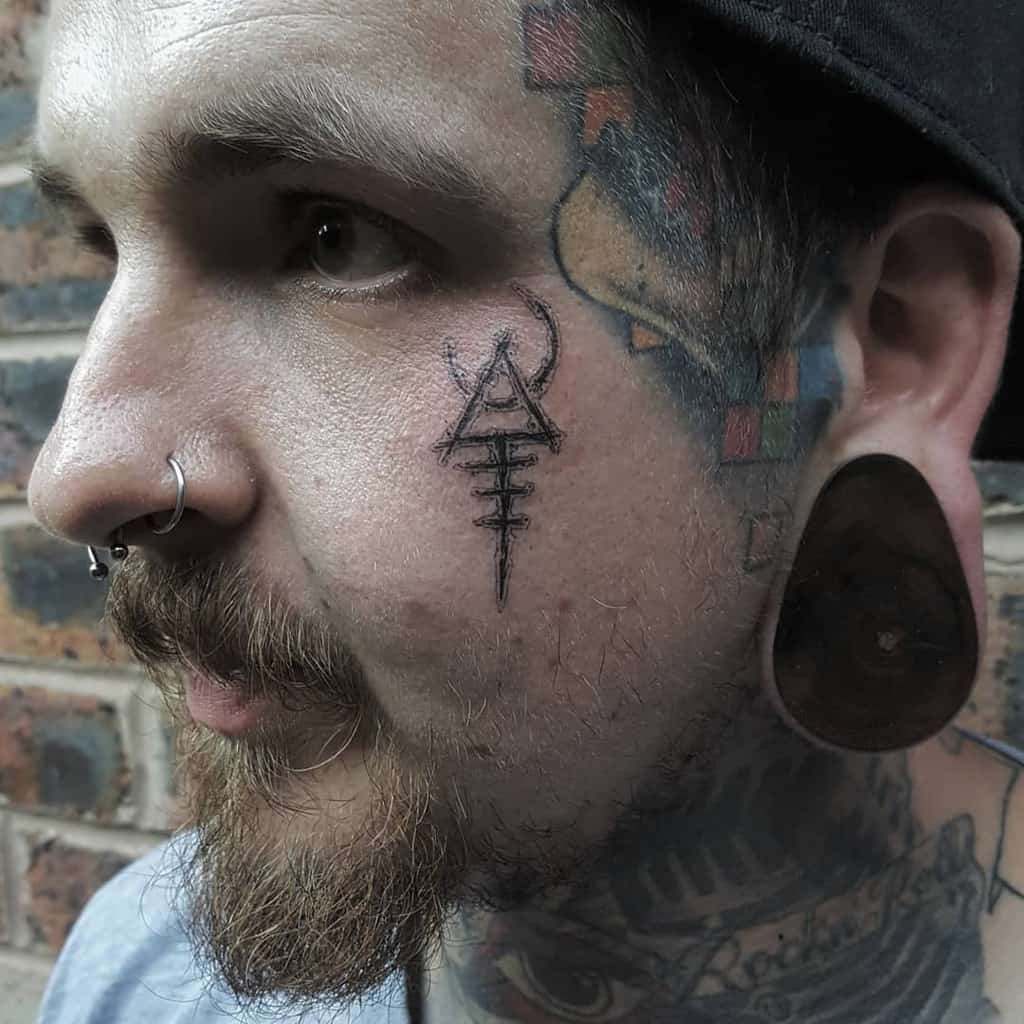 Tribal-style geometric tattoo on the cheek featuring a triangular design and lines below