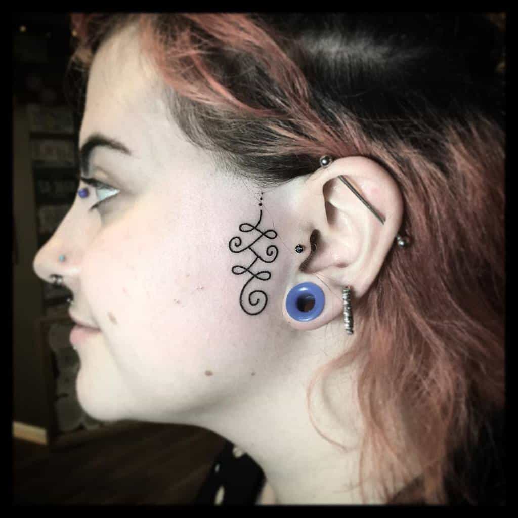 Delicate, swirling tribal-style tattoo behind the ear, featuring a dotted line and flowing curves