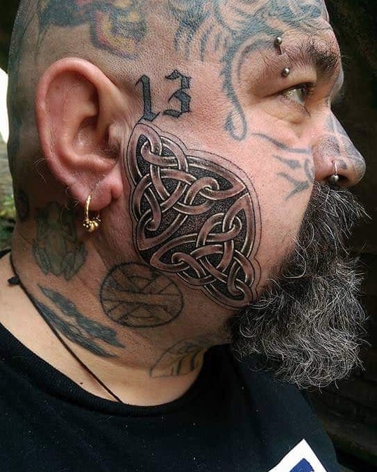 Celtic knot tribal tattoo covering the cheek, surrounded by additional tattoos on the head and neck