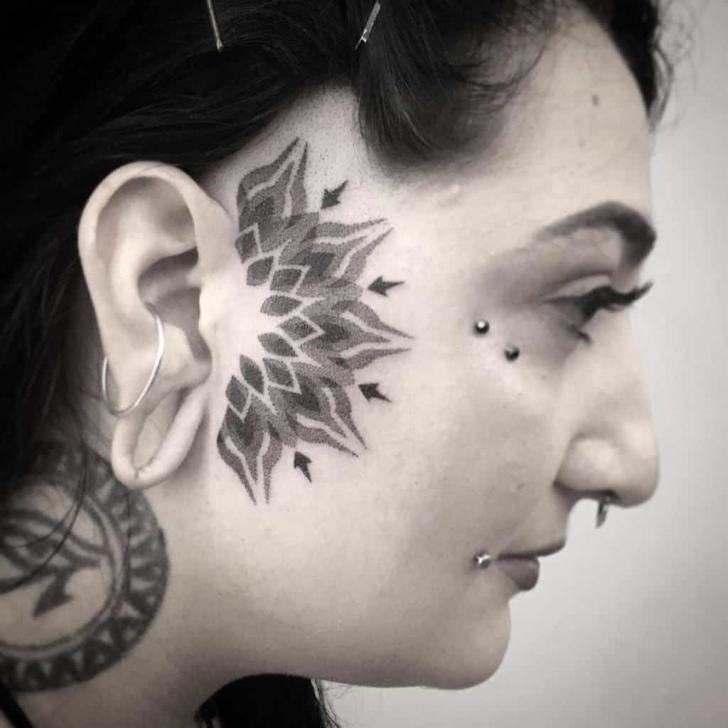 Bold, geometric tribal tattoo on the cheek, featuring a symmetrical, layered pattern extending from the ear