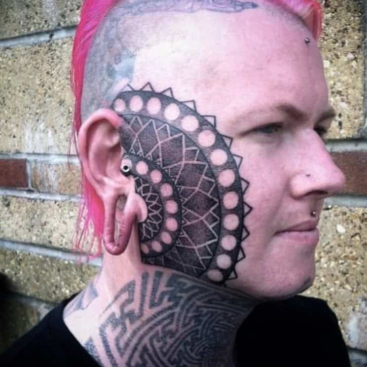 Mandala-inspired tribal tattoo covering the cheek and extending towards the ear, featuring circular and geometric patterns