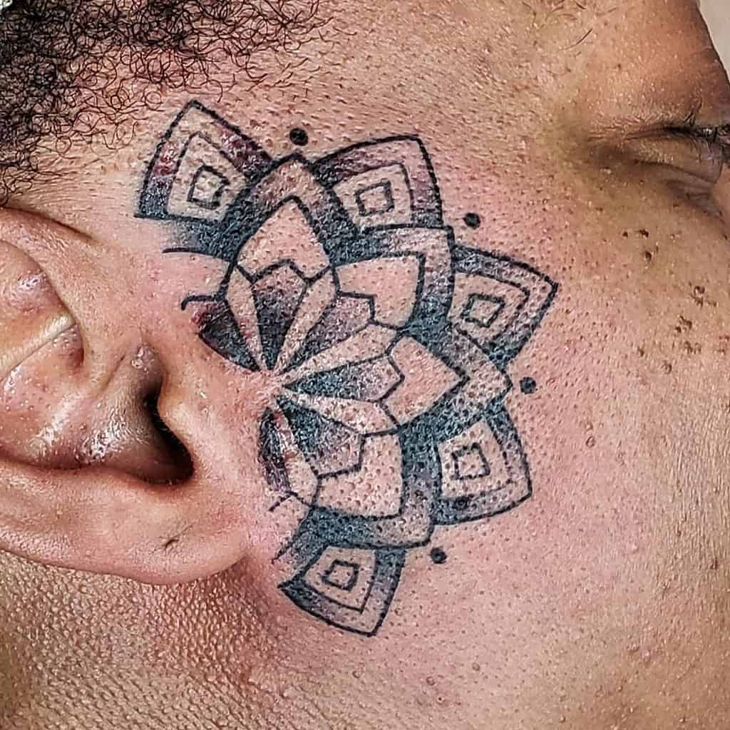 Geometric mandala-style tribal tattoo on the cheek, featuring layered square and petal-like patterns