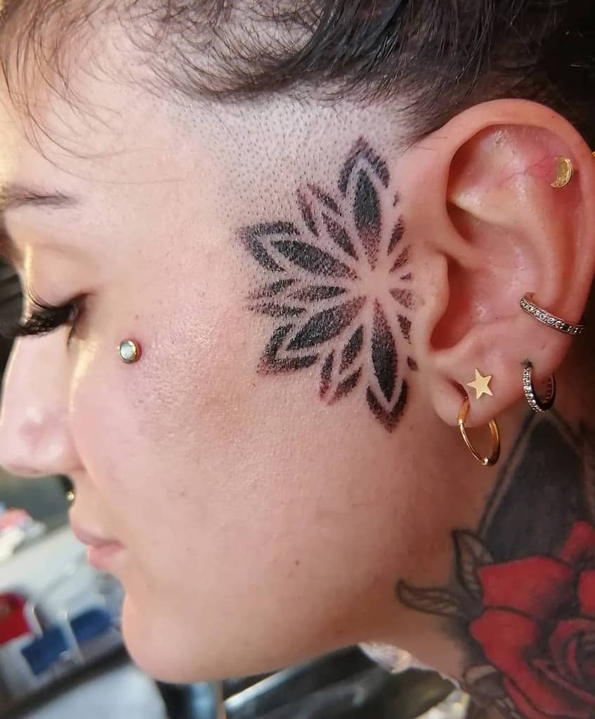 Bold, petal-shaped tribal tattoo on the cheek, radiating from the ear, with intricate shading and sharp edges