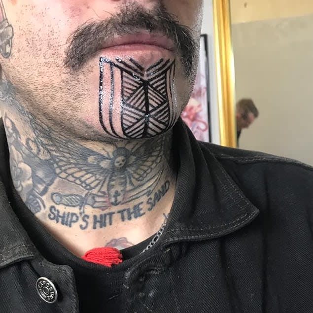 Geometric tribal tattoo on the chin, featuring symmetrical lines and patterns, complemented by tattoos on the neck