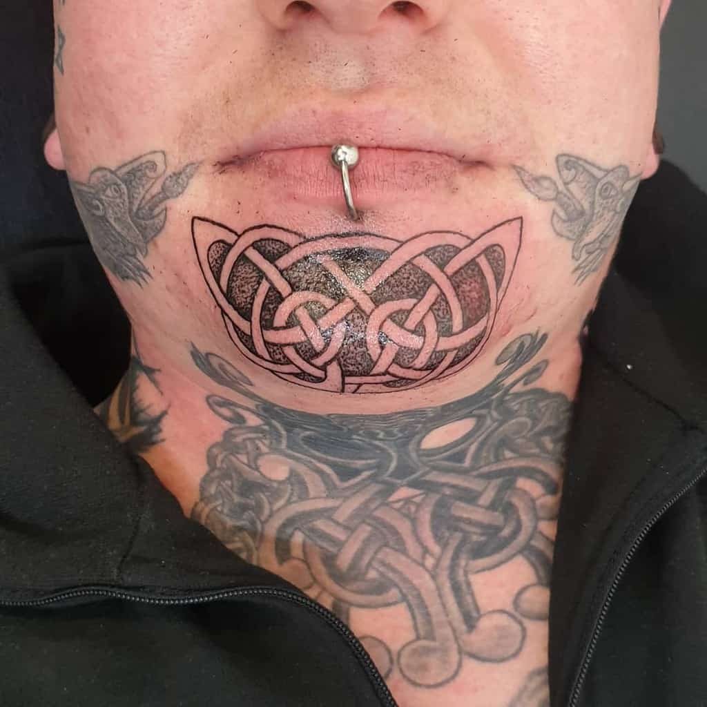 Celtic knot tribal tattoo on the chin, extending from the lower lip, paired with additional knotwork tattoos on the neck