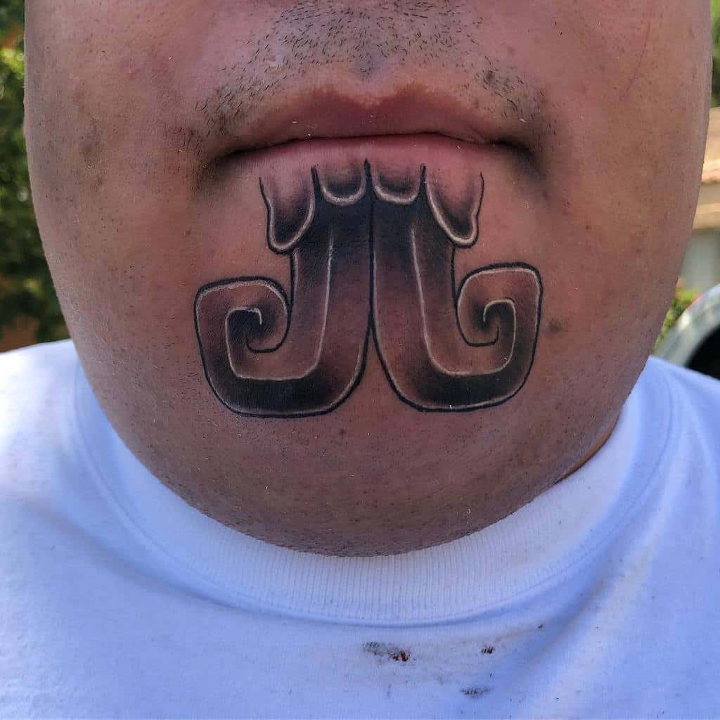 Bold, symmetrical tribal tattoo on the chin, featuring curved and flowing lines forming a stylized pattern
