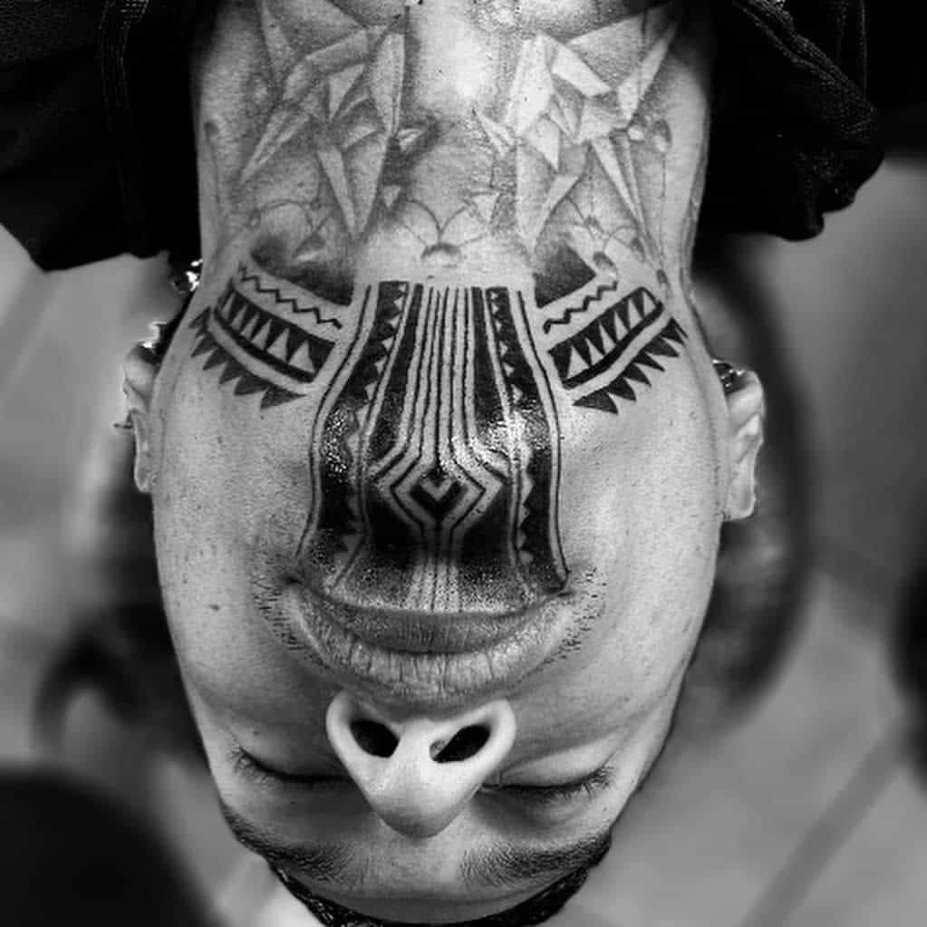 Intricate tribal tattoo covering the chin, extending to the lower lip and neck, featuring bold geometric patterns and symmetrical lines