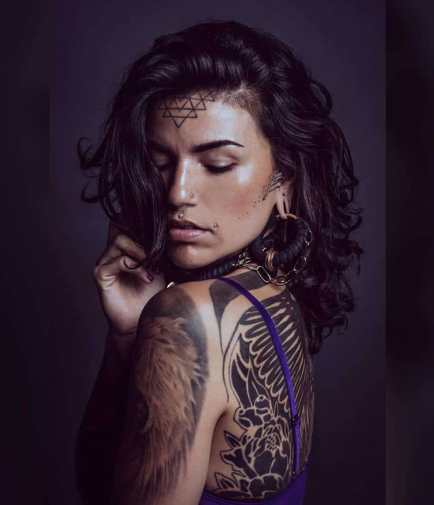 Geometric tribal tattoos on the forehead and face, featuring triangles and dot work