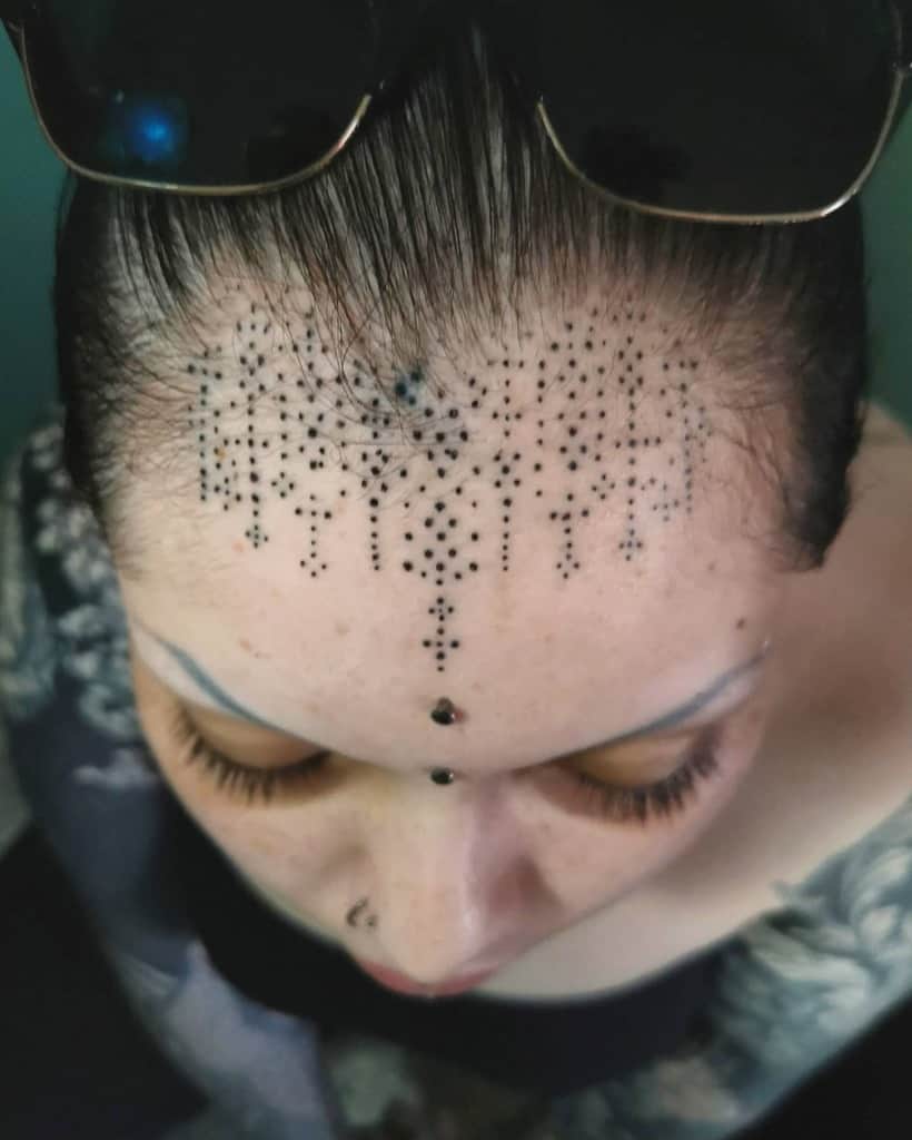 Dotted tribal tattoo on the forehead, featuring intricate patterns and small dot clusters extending towards the center, complemented by a central dot