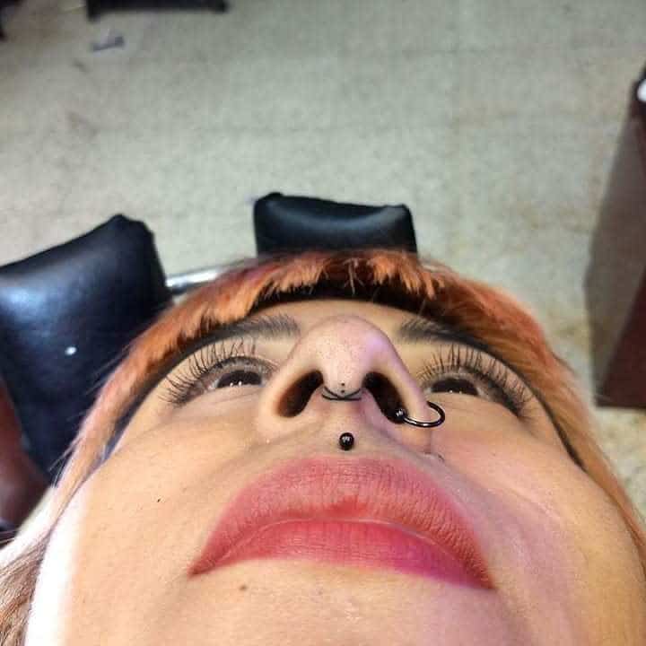Woman's nose tattoo with a small curved design between the nostrils, accompanied by a septum ring and lip piercing