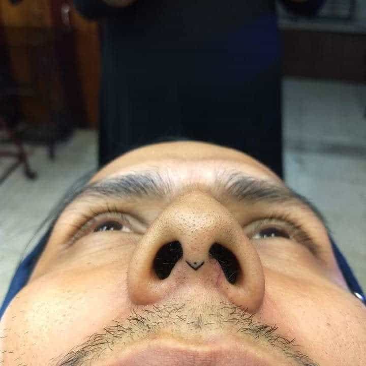 Man's nose tattoo with a small triangular design between the nostrils, showcasing a minimalist look