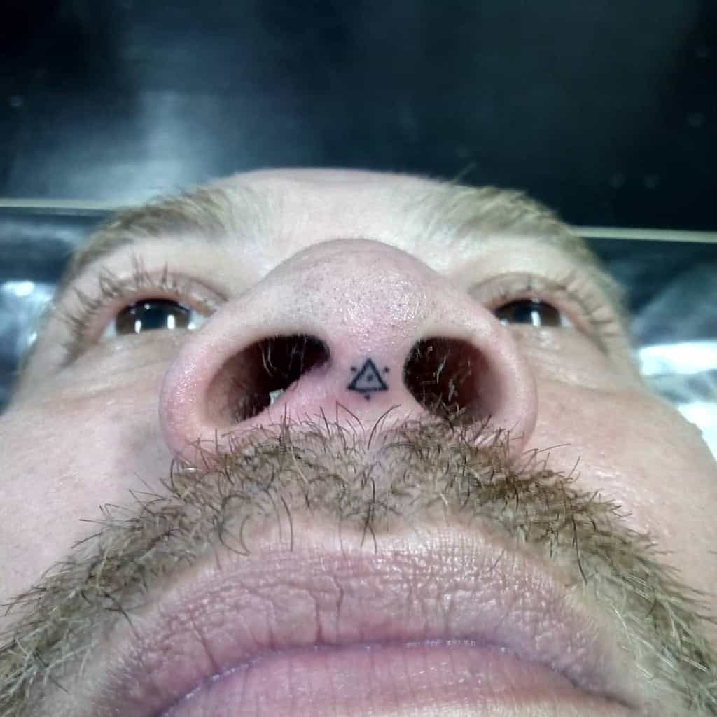 Man's nose with a small triangular tattoo between the nostrils