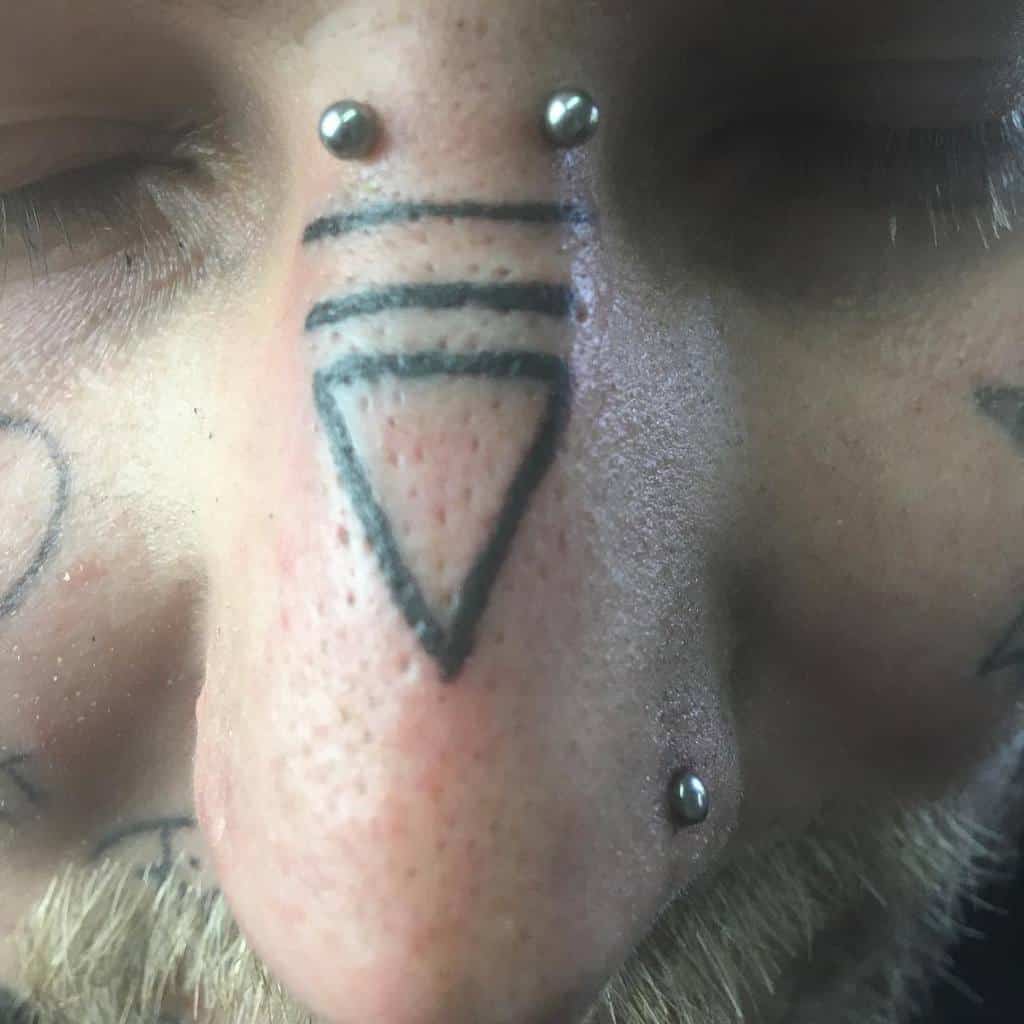 Man's nose tattoo featuring a bold triangle with three parallel lines above, alongside nose piercings