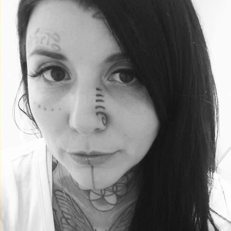 Woman with tribal-style facial tattoos, including a spiral design on her nose and dot patterns near the eyes