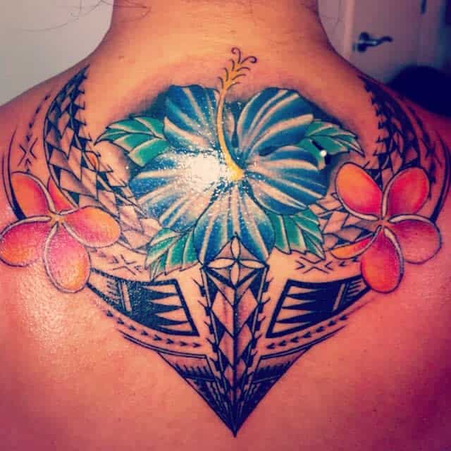 Vibrant tattoo of a blue hibiscus surrounded by red-orange plumeria flowers and geometric tribal patterns on a back