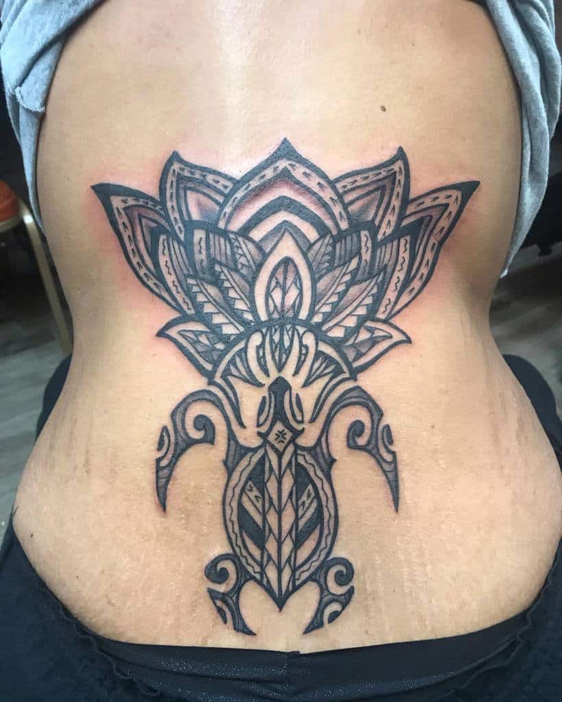Ornate black tattoo on lower back featuring a symmetrical design with lotus and abstract patterns