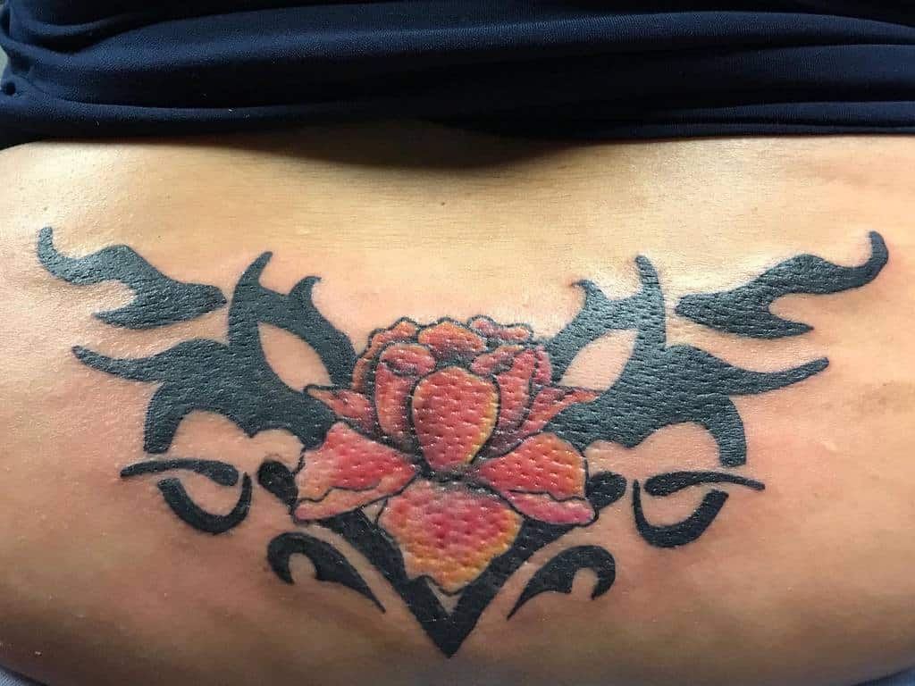 A rose tattoo with black tribal designs on lower back