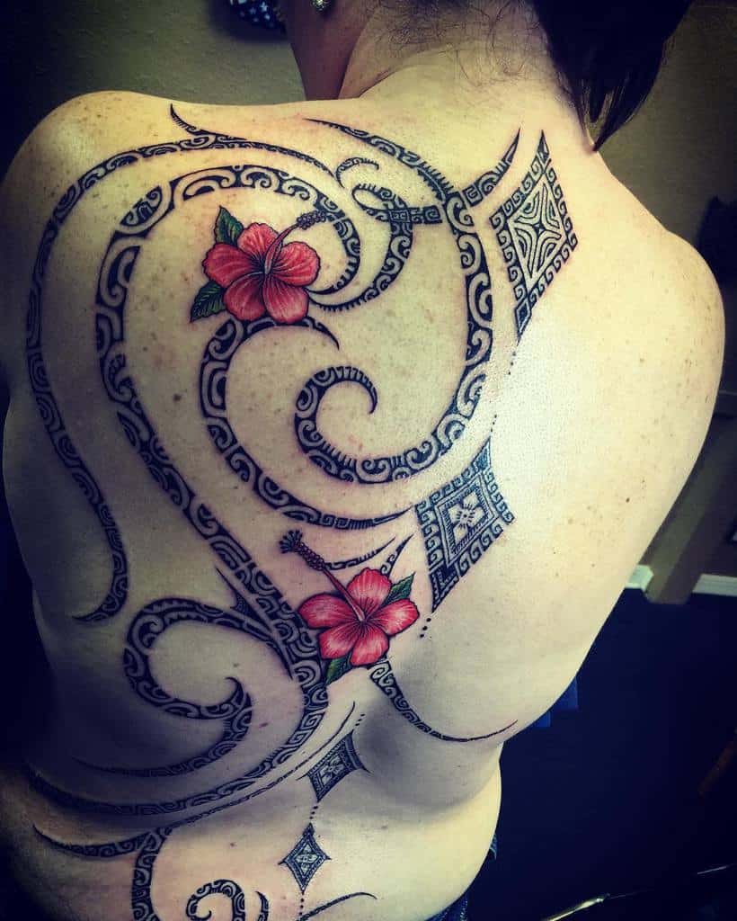 Intricate tribal-style tattoo with red hibiscus flowers covering a woman's back