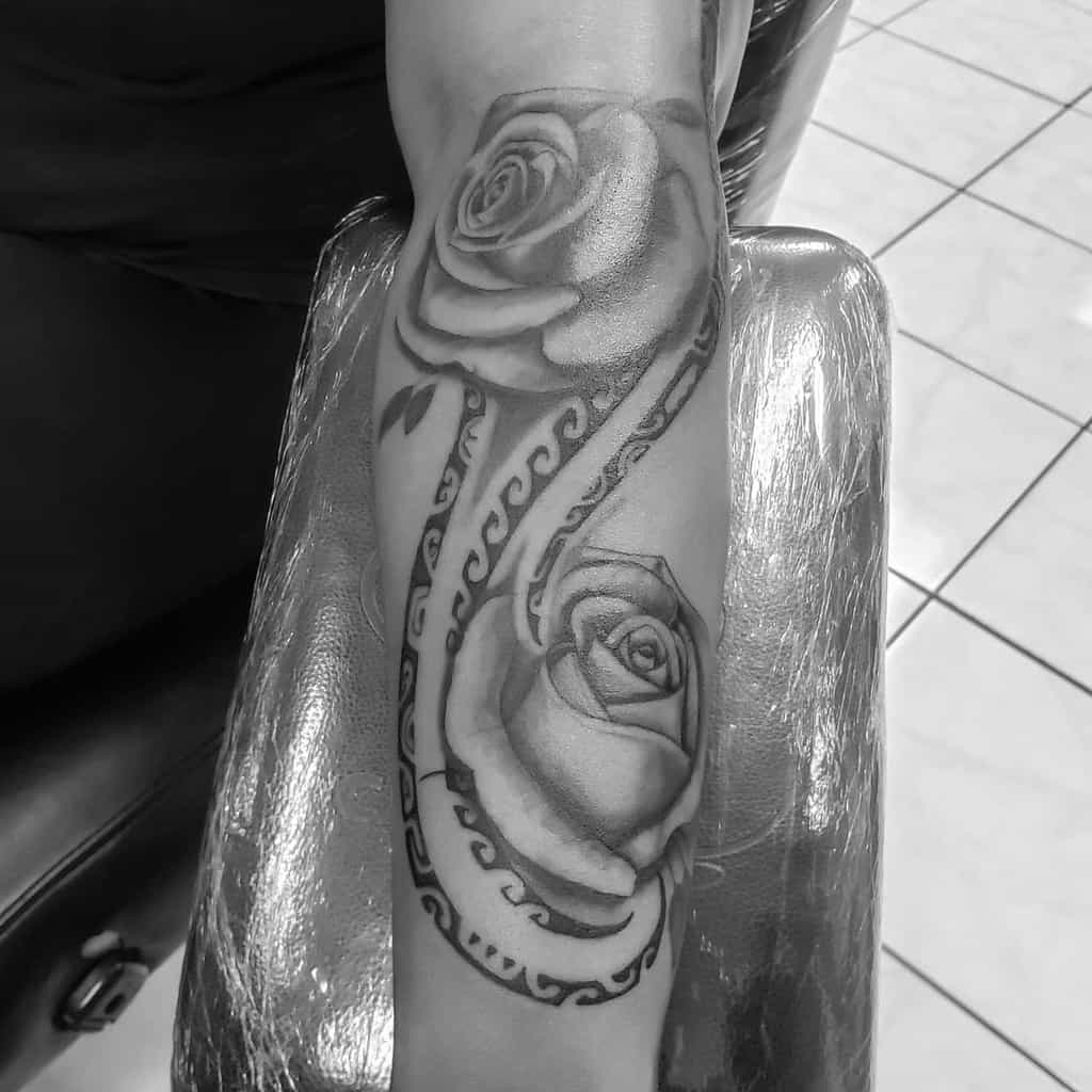 Arm tattoo of two realistic roses with swirling, tribal style vines in black and gray ink
