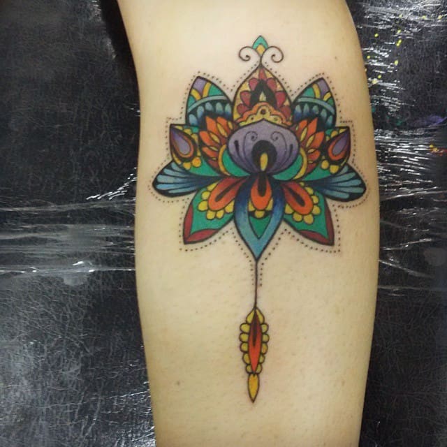 Colorful mandala tattoo on upper arm featuring intricate patterns, a central lotus design, and a dangling feather