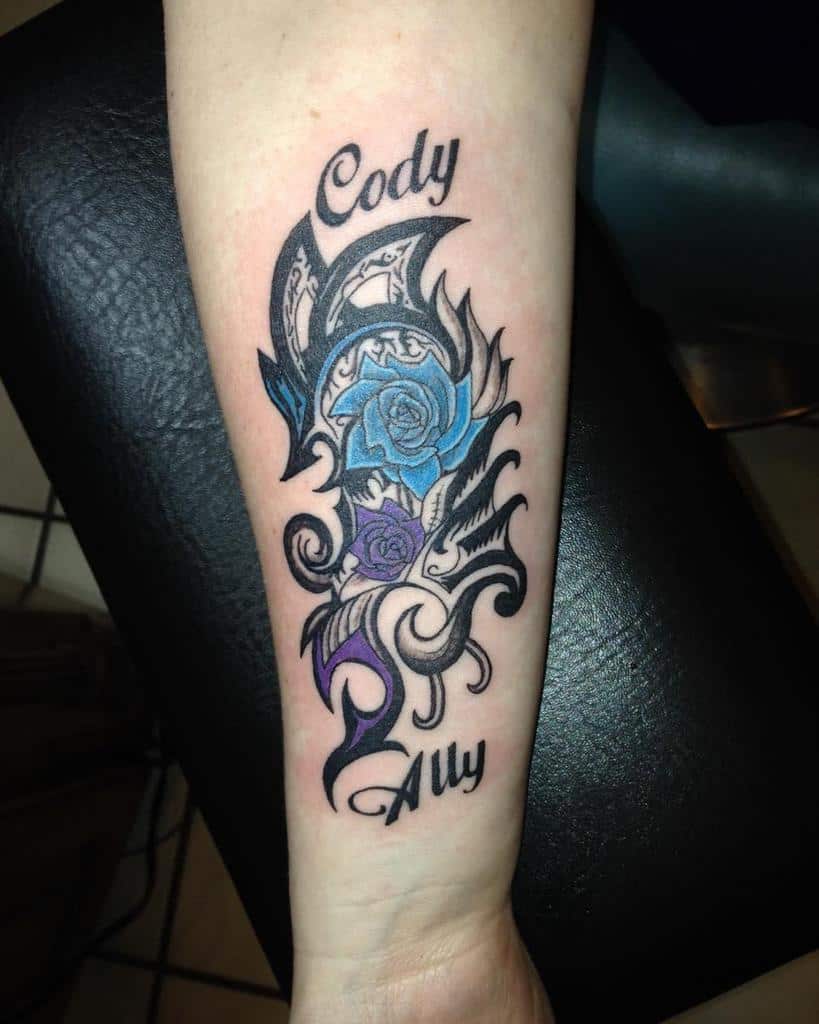 Tattoo on forearm with blue and purple roses, tribal patterns, and the names "Cody" and "Ally"