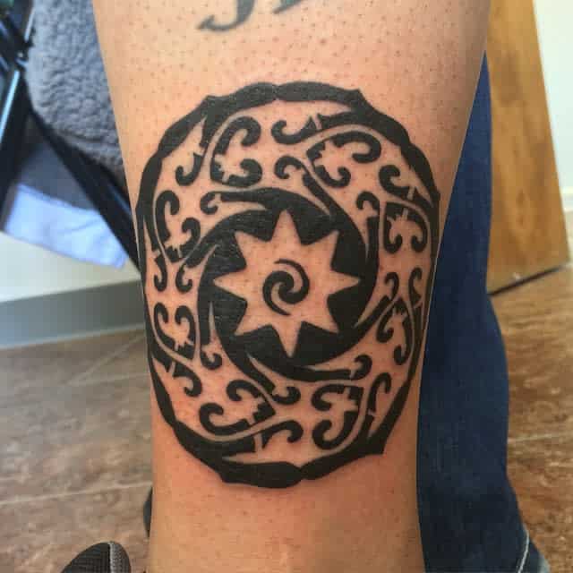 Tattoo of a bold, black circular design with a star and swirling patterns on a leg