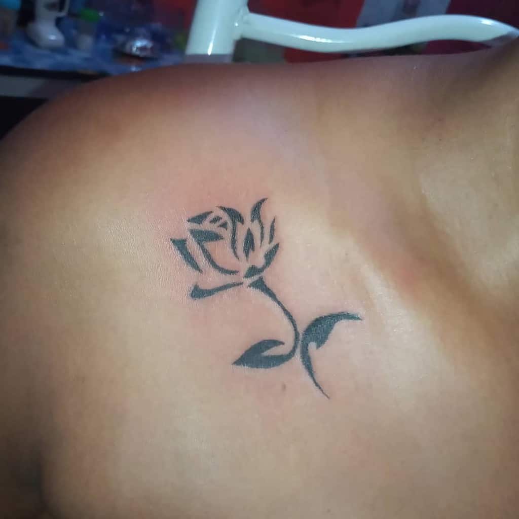A black rose tattoo on a shoulder, showcasing a simple design with leaves and a stem