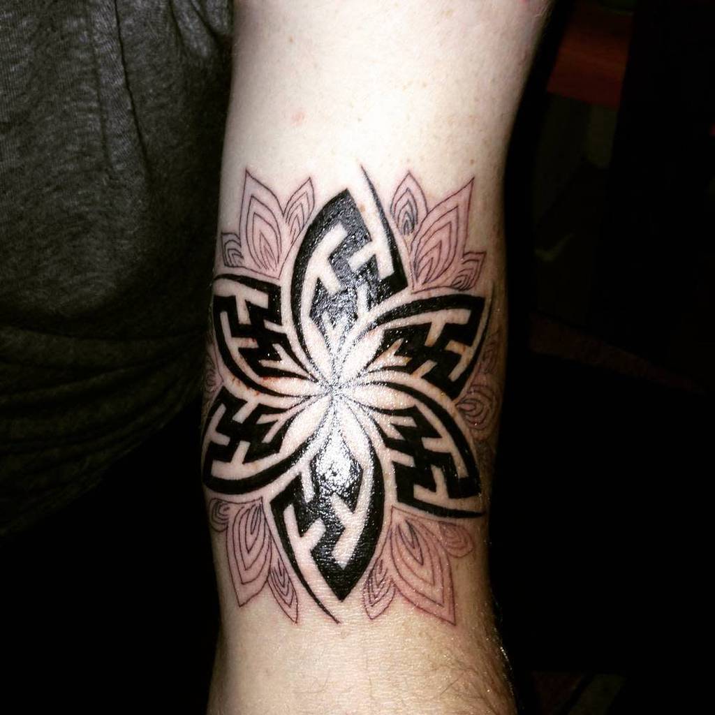 Intricate upper arm tattoo featuring a bold tribal flower design with geometric patterns and layered petal detailing