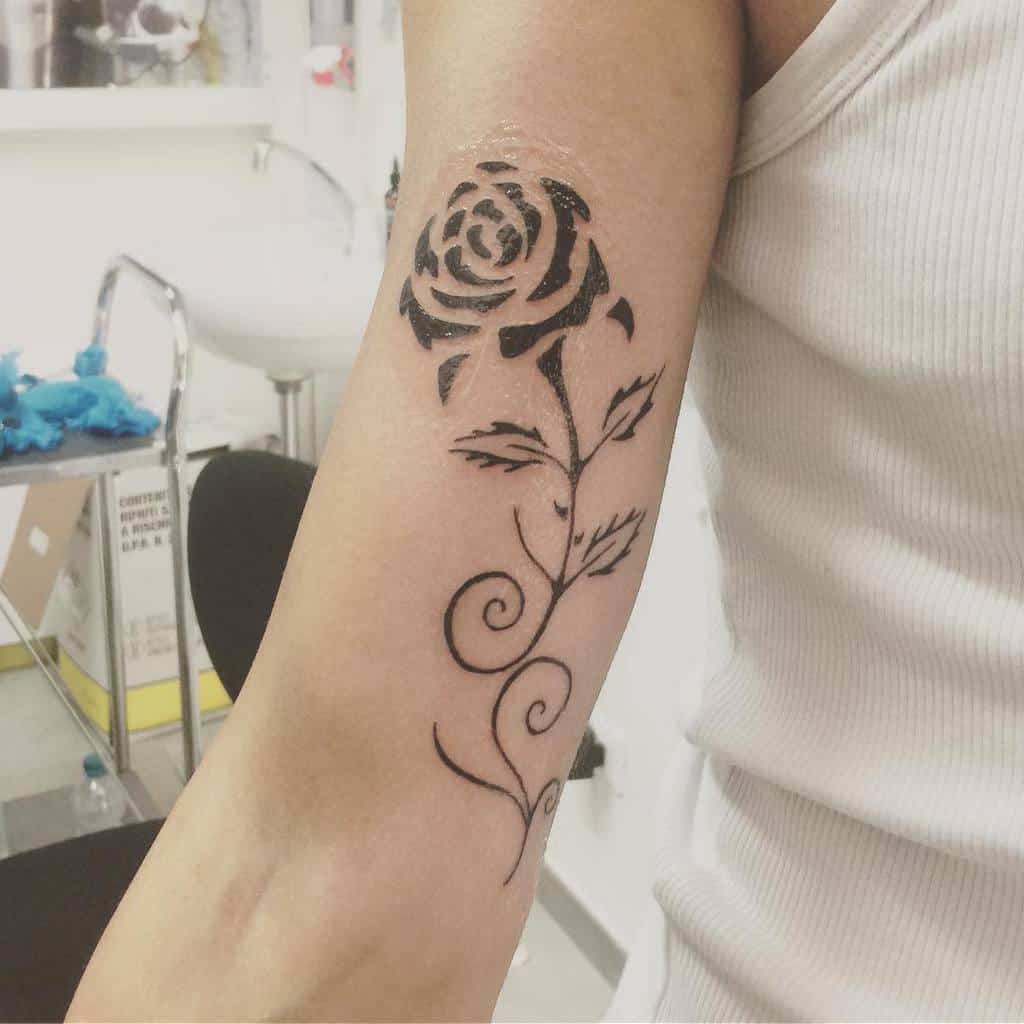 Black ink rose tattoo with leaves and swirls on a woman's upper arm