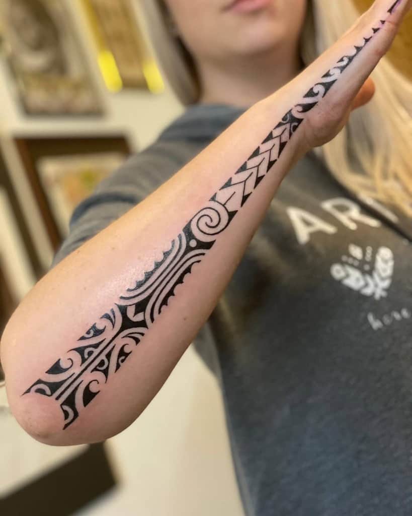 Forearm tattoo with intricate black tribal design, featuring swirls and geometric patterns