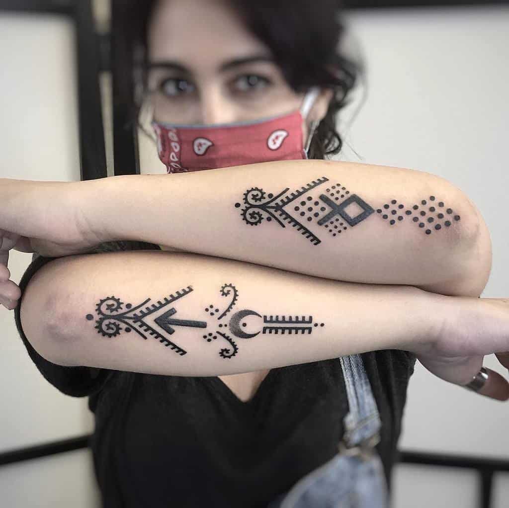Two symmetrical tribal-style forearm tattoos featuring geometric shapes, dots, and bold black lines on a woman's arms