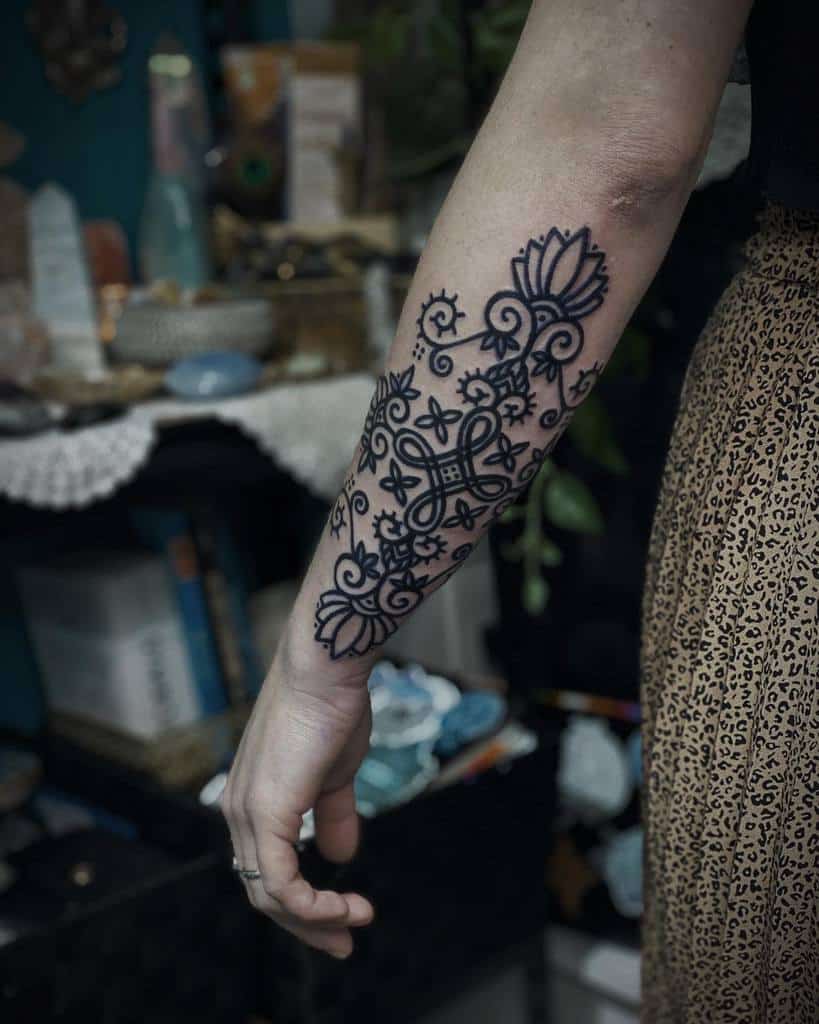 Detailed forearm tattoo with bold black lines, featuring floral patterns, spirals, and intricate geometric elements