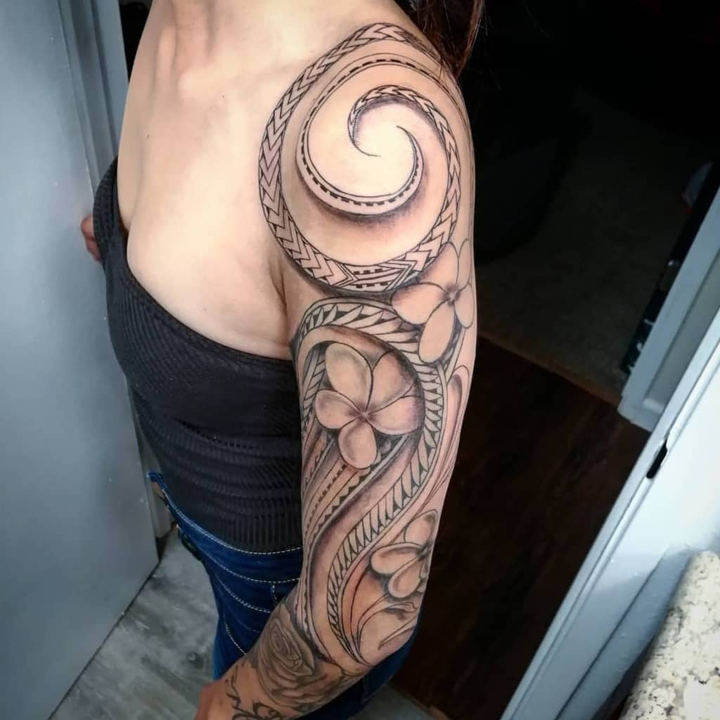Full sleeve tribal tattoo with bold spirals, detailed patterns, and large floral elements, extending from shoulder to wrist
