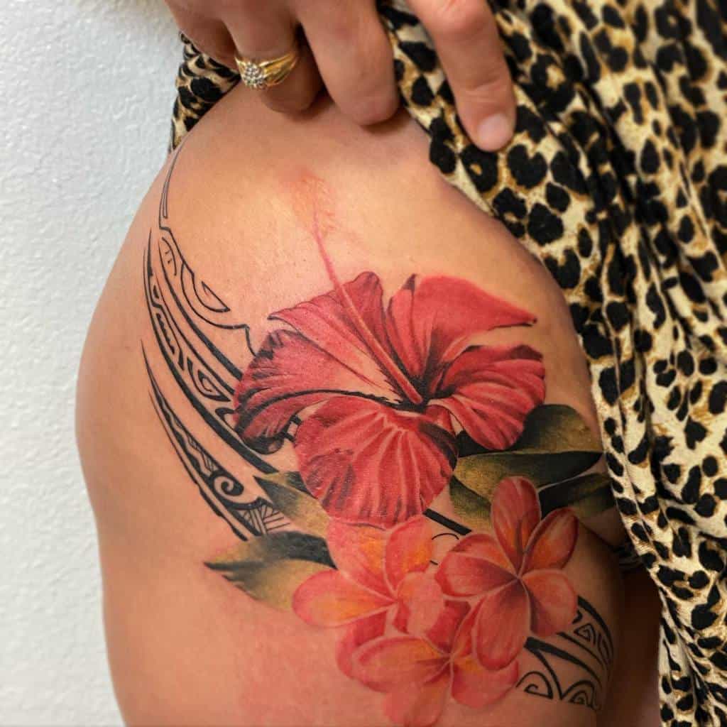 A colorful hibiscus and plumeria tattoo with tribal patterns on a hip and upper thigh