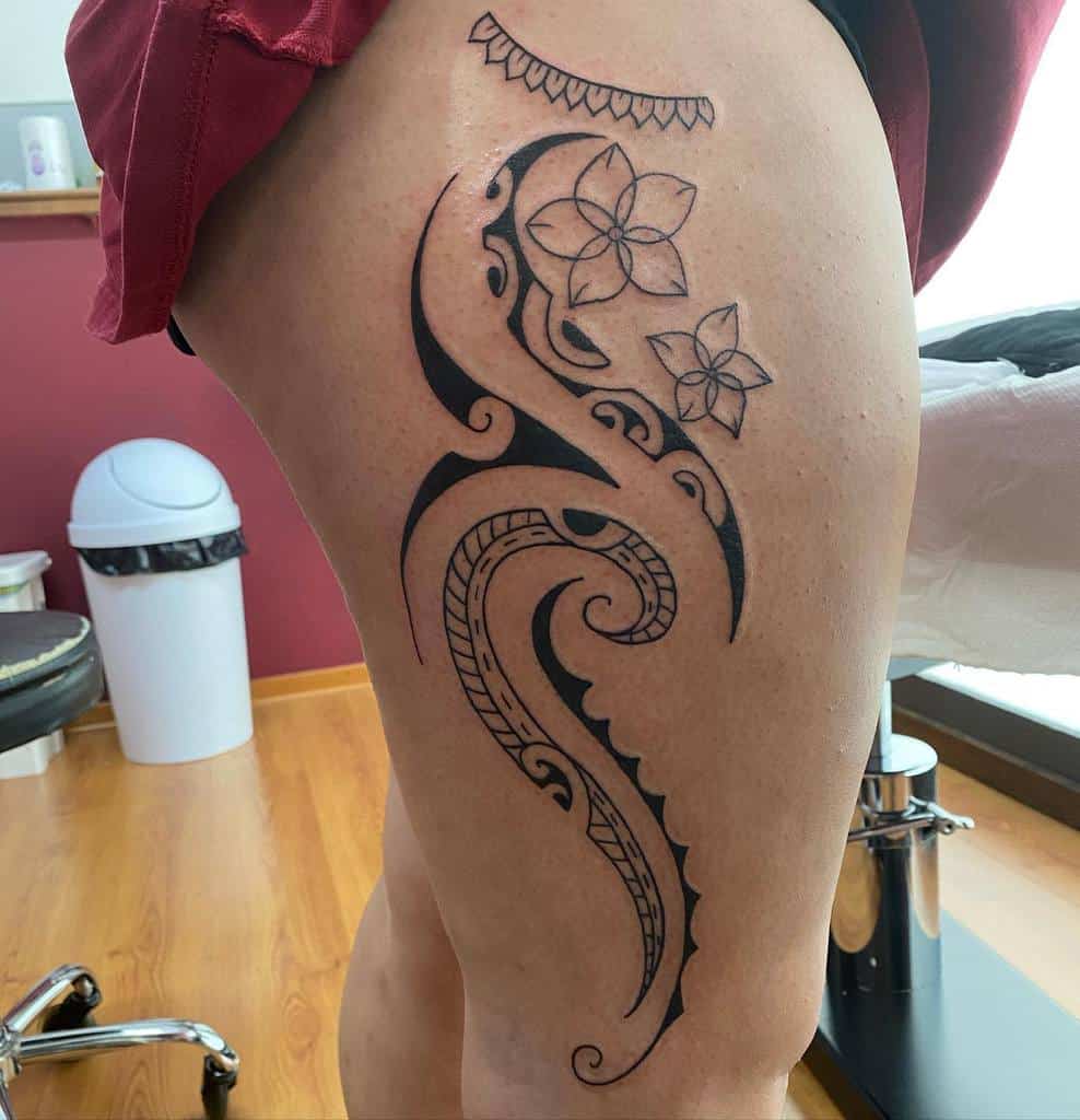 Ornate black tribal tattoo with floral elements on a woman's thigh