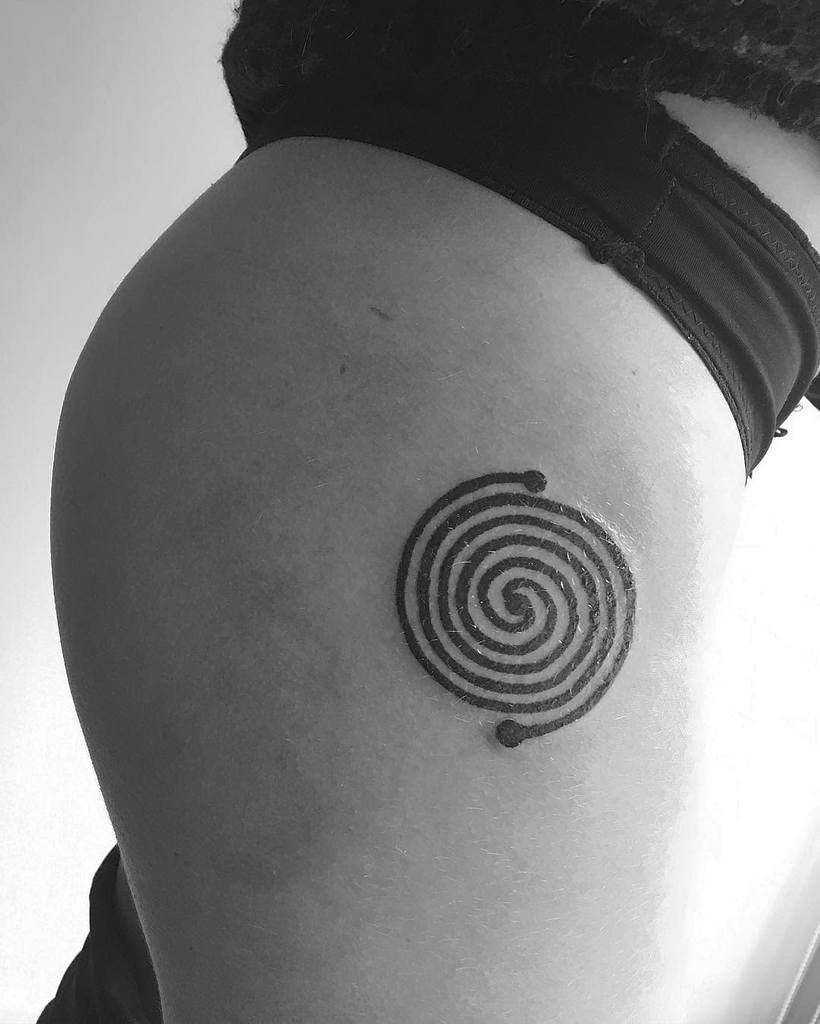 A black spiral tattoo on a woman's hip, surrounded by three dots