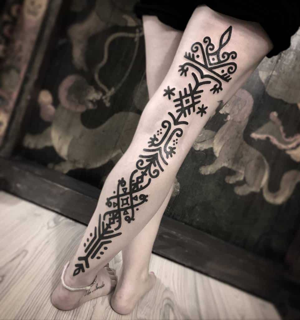 A leg with intricate black tribal tattoos extends from ankle to thigh, featuring patterns and a crown design