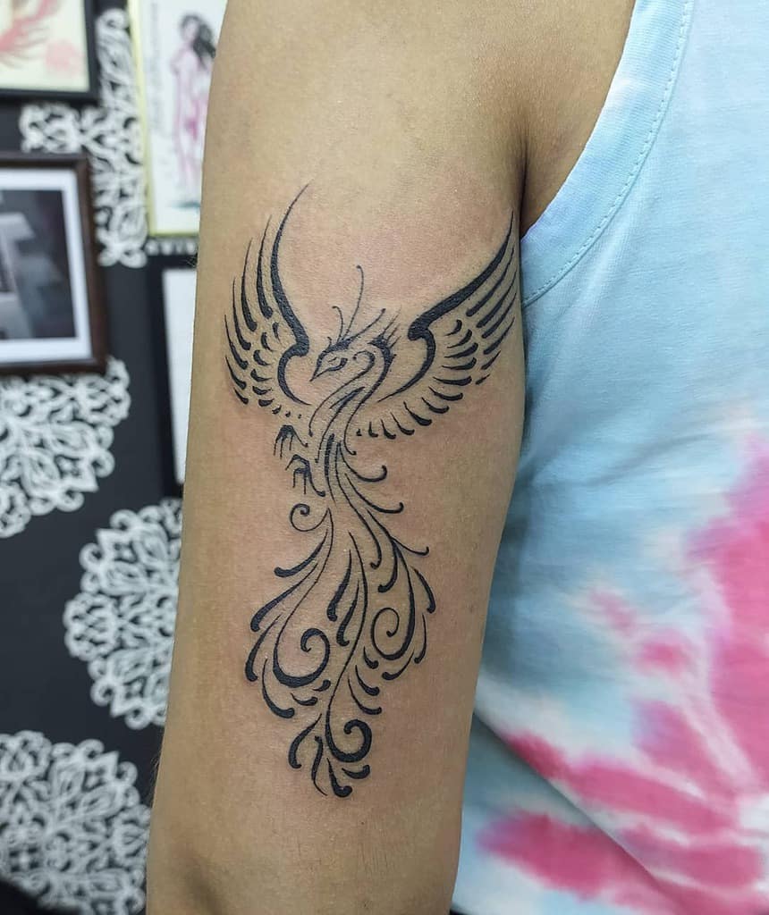 A phoenix tattoo on a person's upper arm, with detailed black ink tribal design