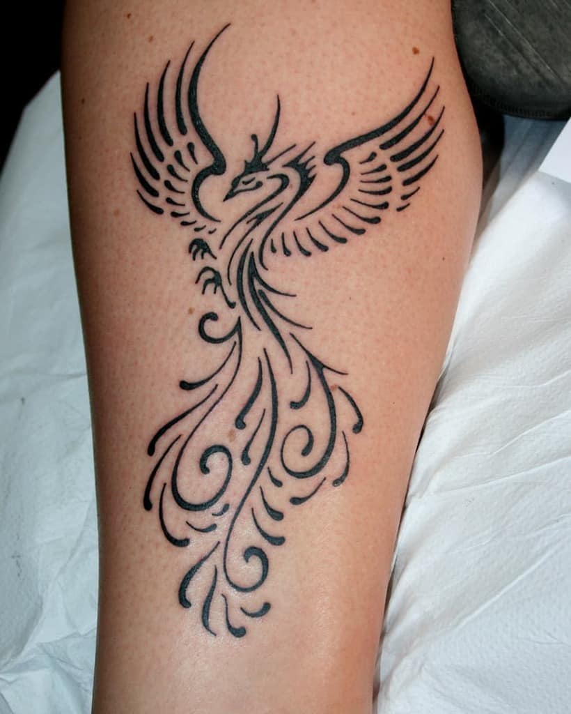Tattoo of a stylized tribal phoenix with intricate wings and swirling tail on a person's forearm