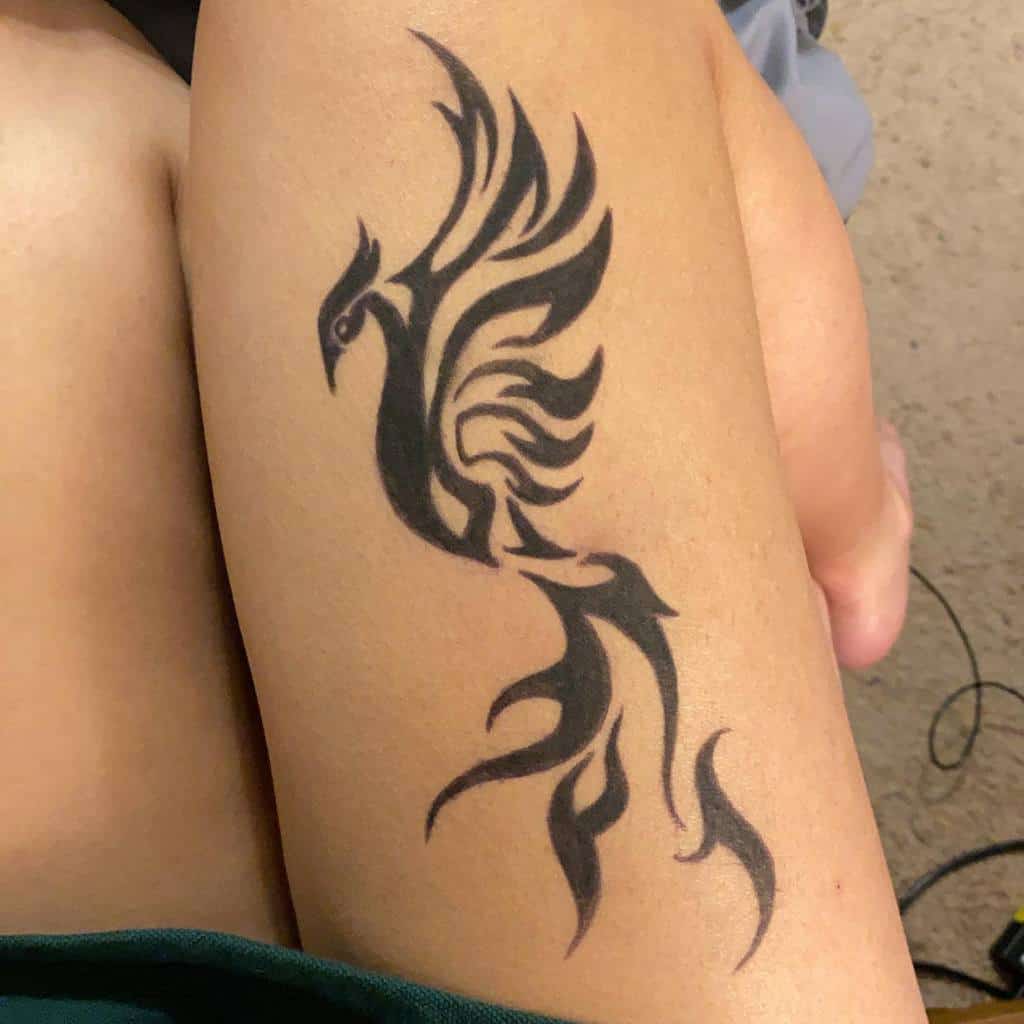 Black tribal-style phoenix tattoo on an upper leg and thigh