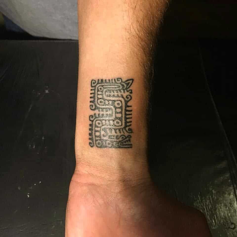Minimalist wrist tattoo of Quetzalcoatl in a tribal pattern with geometric shapes